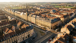 Vue aérienne réaliste de Dijon montrant le centre historique, les toits bourguignons et les lignes de tramway baignés par la lumière dorée de fin d’après-midi.